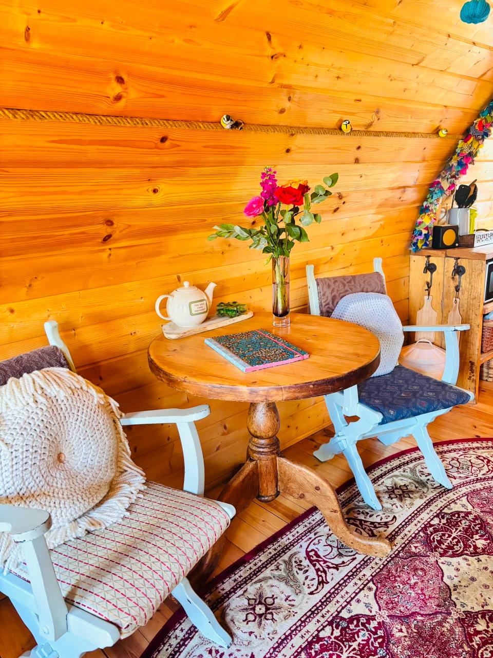 Inside the hobbit house — round tea table with fresh roses, teapot and painted chairs