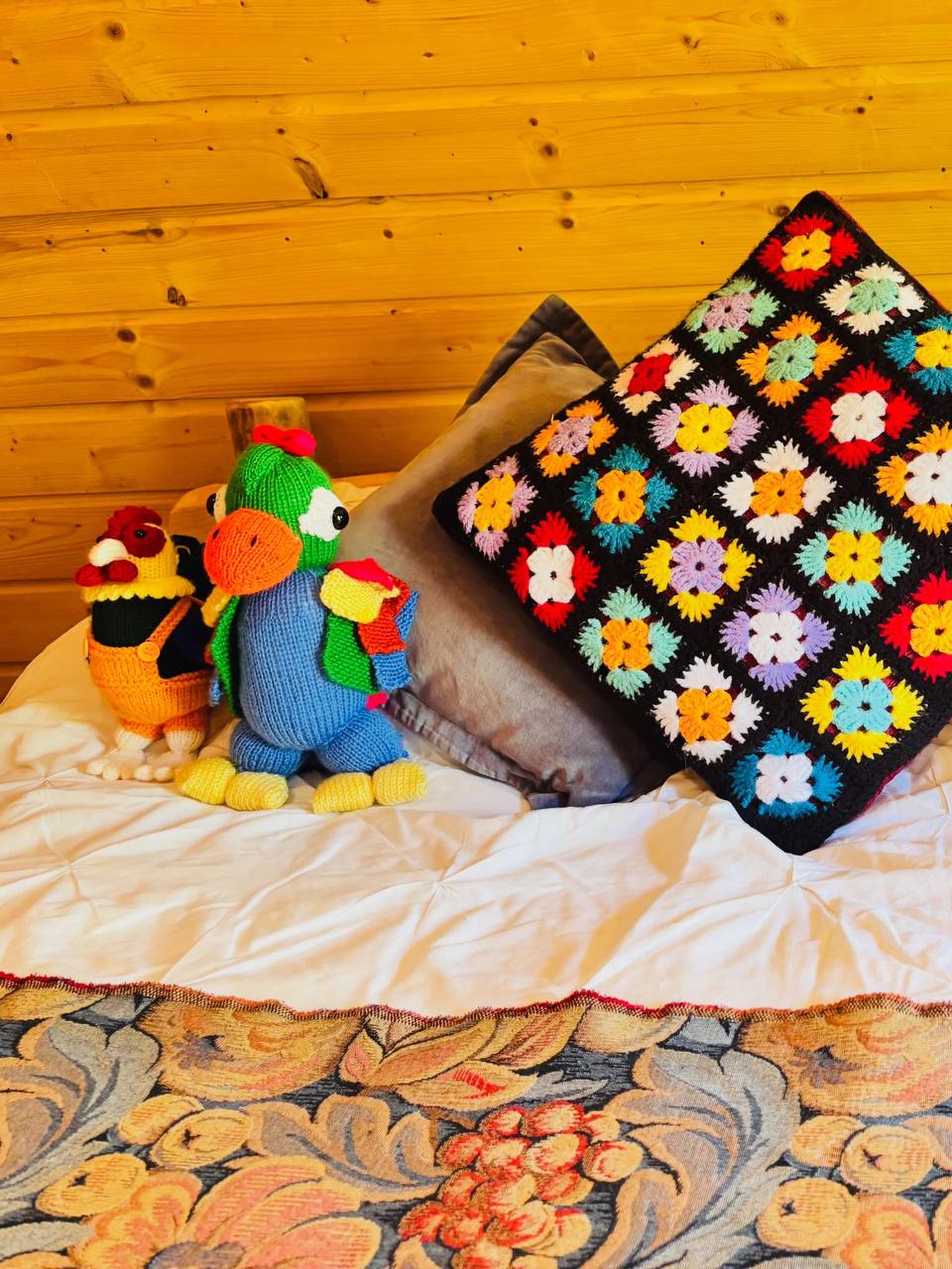 Hand-knitted parrot and hen beside a crochet flower cushion on the bed