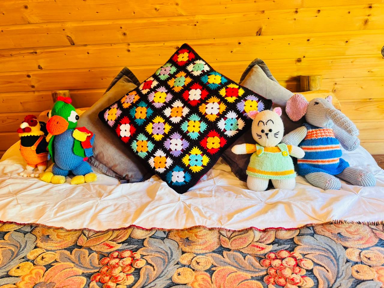 Knitted animals and a granny-square cushion on the bed in the hobbit house